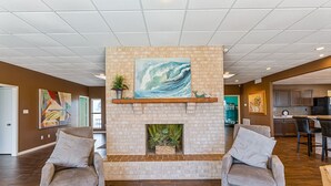 A lobby with a brick fireplace, two armchairs, and a dining area.