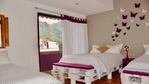 Une chambre avec deux lits, une fenêtre avec des rideaux, une vue sur les montagnes et des autocollants décoratifs représentant des papillons sur les murs.