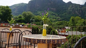 Une terrasse avec une table ronde et des chaises, un vase rempli de fleurs et un paysage montagneux en arrière-plan.