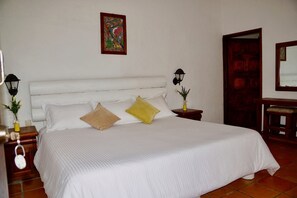 A neatly made bed with white bedding and two pillows, a small table with a lamp, and a painting on the wall.