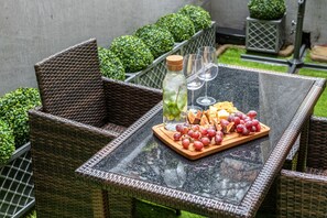 A glass-top table with a wooden board holding grapes and cheese, a bottle of water, and two glasses.