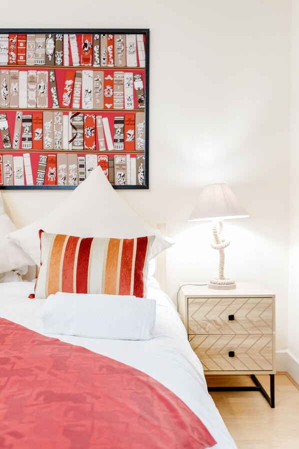A neatly made bed with a striped pillow, a bedside lamp, and a wall-mounted book display.