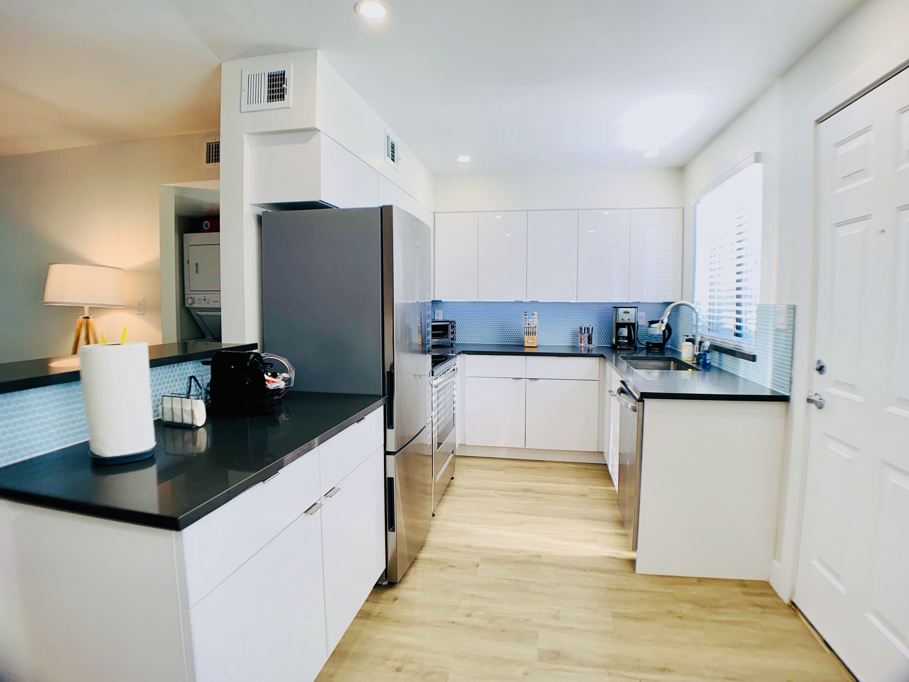 A modern kitchen with white cabinets, a black countertop, and a blue backsplash.