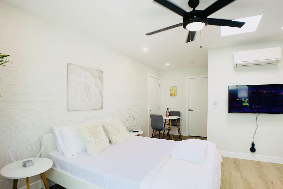 A modern hotel room with a large bed, a ceiling fan, a TV, and a small table with a chair.