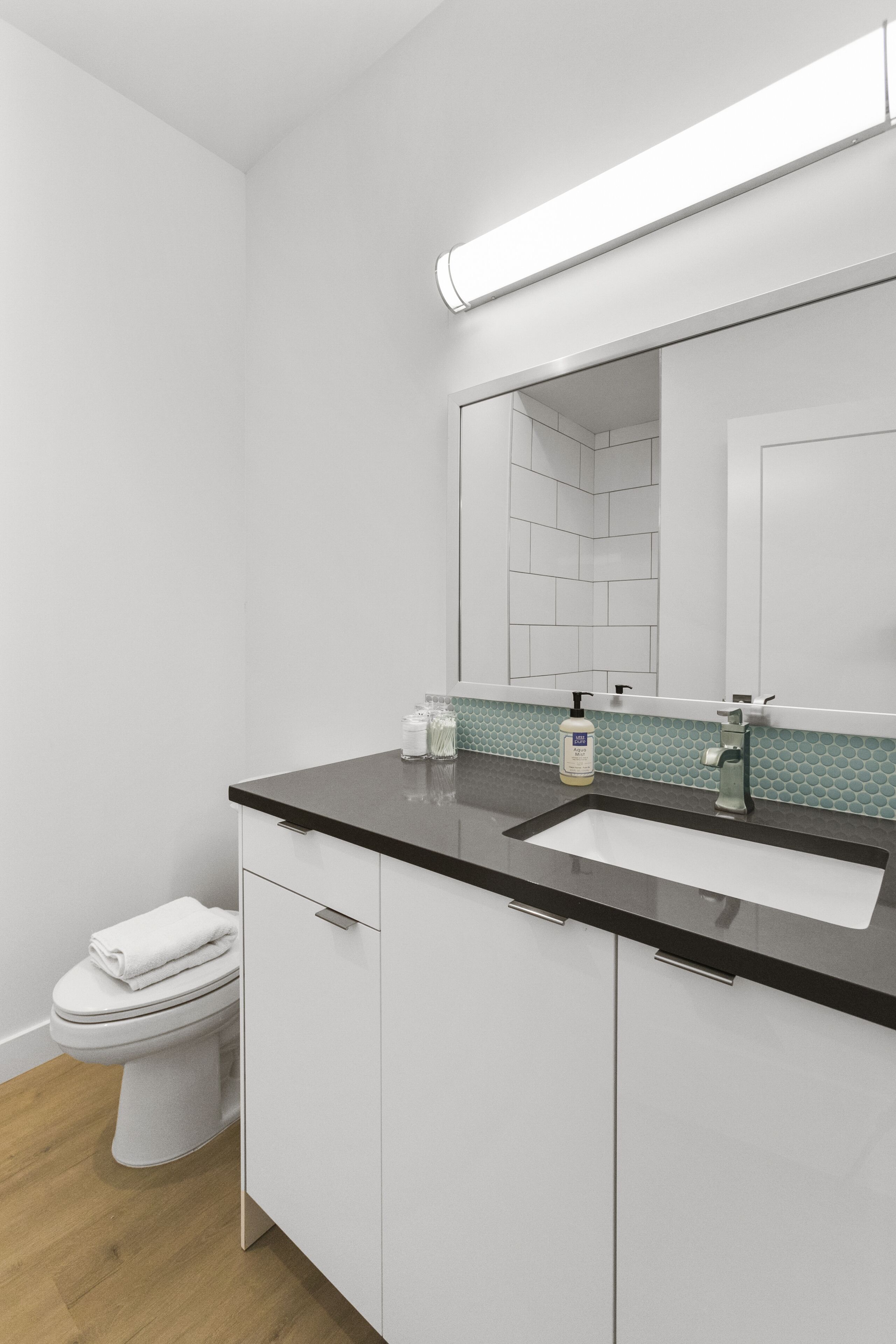 Un baño moderno con un inodoro blanco, un lavamanos con espejo y un dispensador de jabón en la encimera.