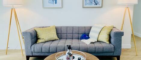 A living room with a grey sofa, two framed abstract artworks, a round coffee table with a tray, and two floor lamps.