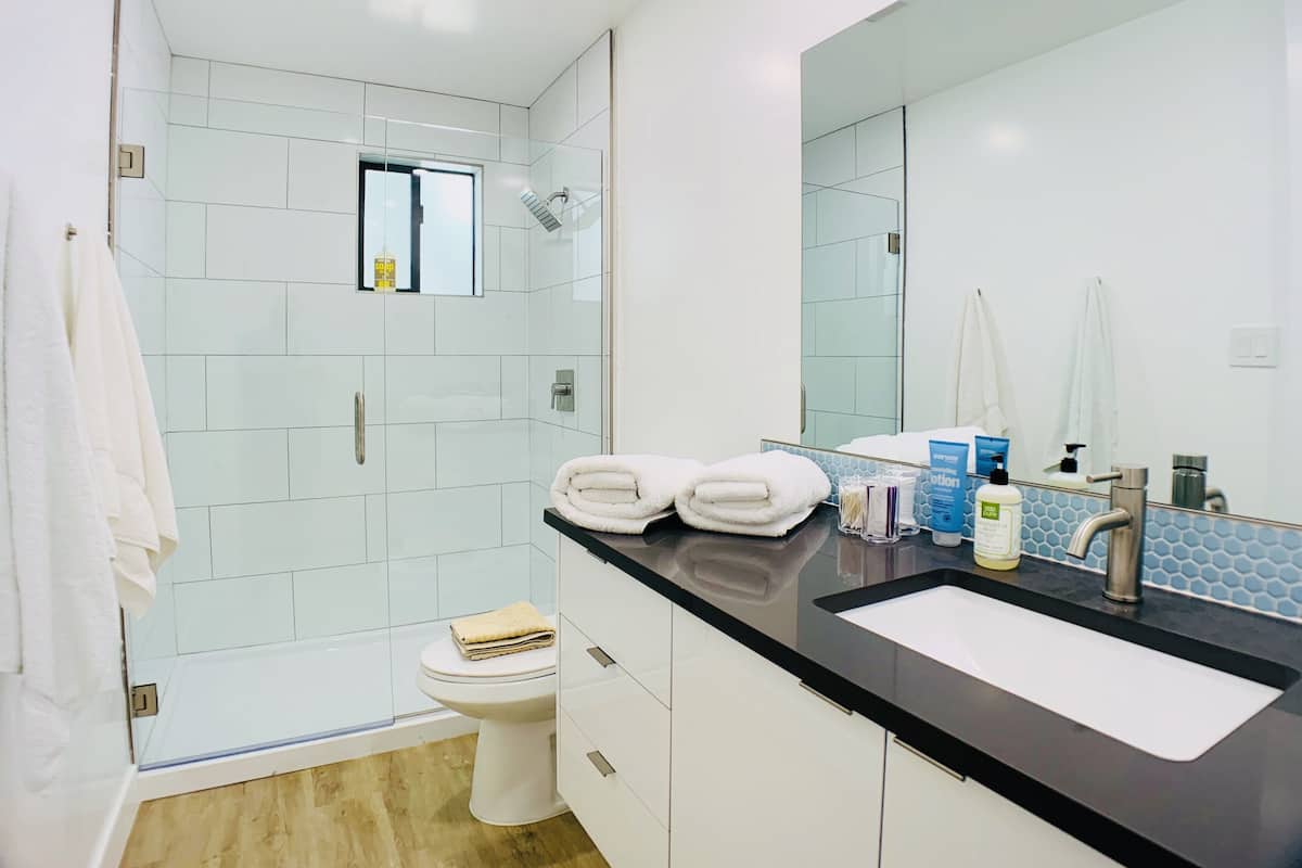 A modern bathroom with a glass shower enclosure, white tiles, a black countertop, and a large mirror.