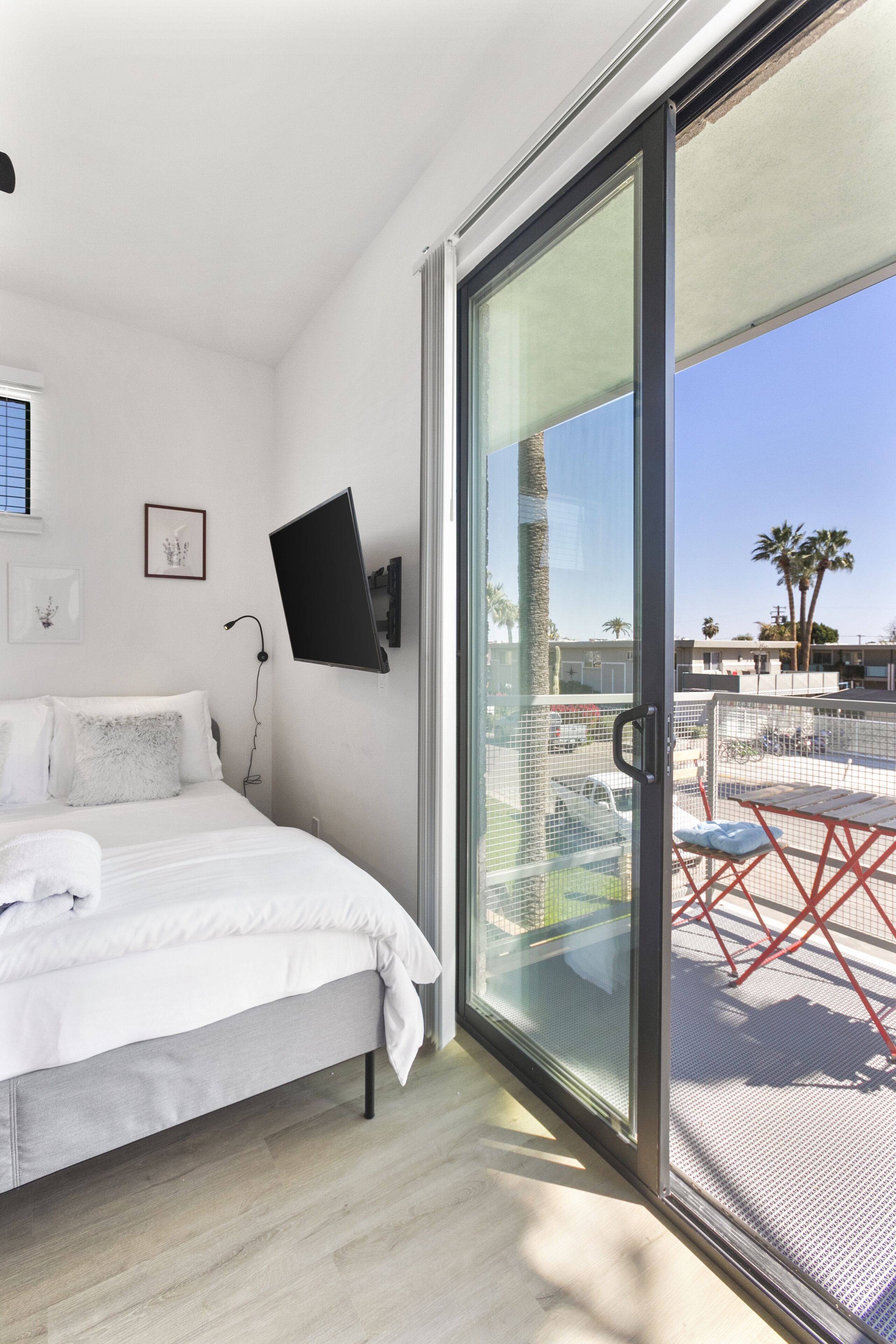 A bedroom with a bed, a TV mounted on the wall, and a sliding glass door leading to an outdoor area with a table and chairs.