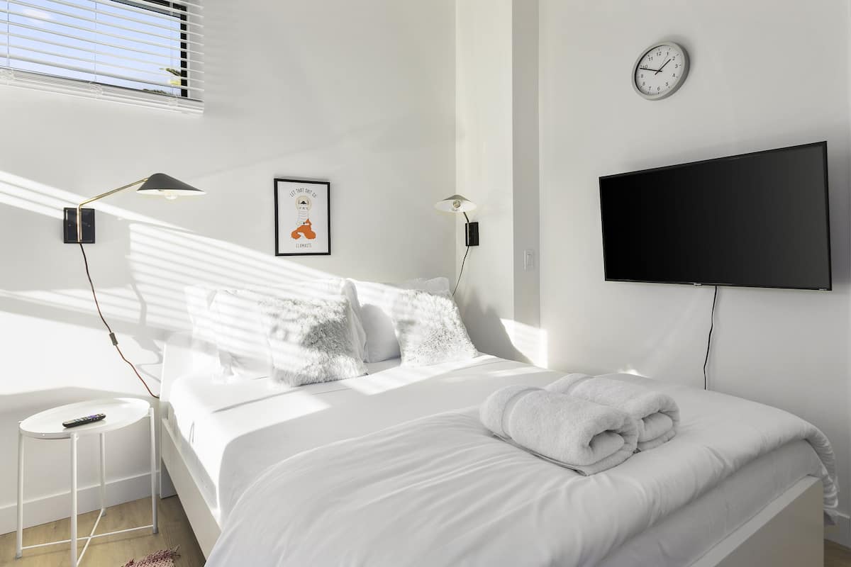 A modern bedroom with a bed, a TV, a clock, and a framed picture on the wall.