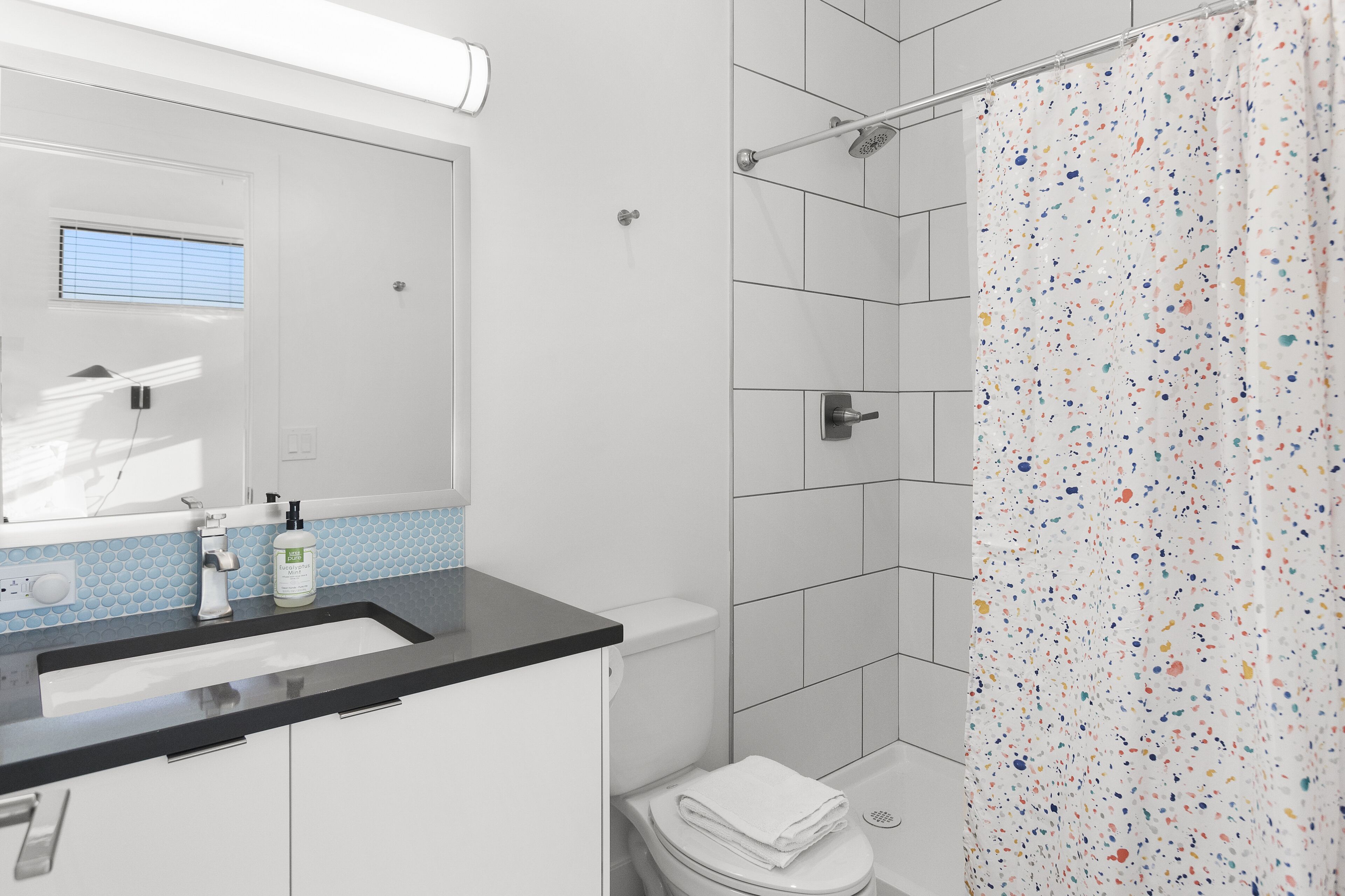Un baño moderno con un lavabo blanco, un inodoro y una ducha con cortina de baño de colores.
