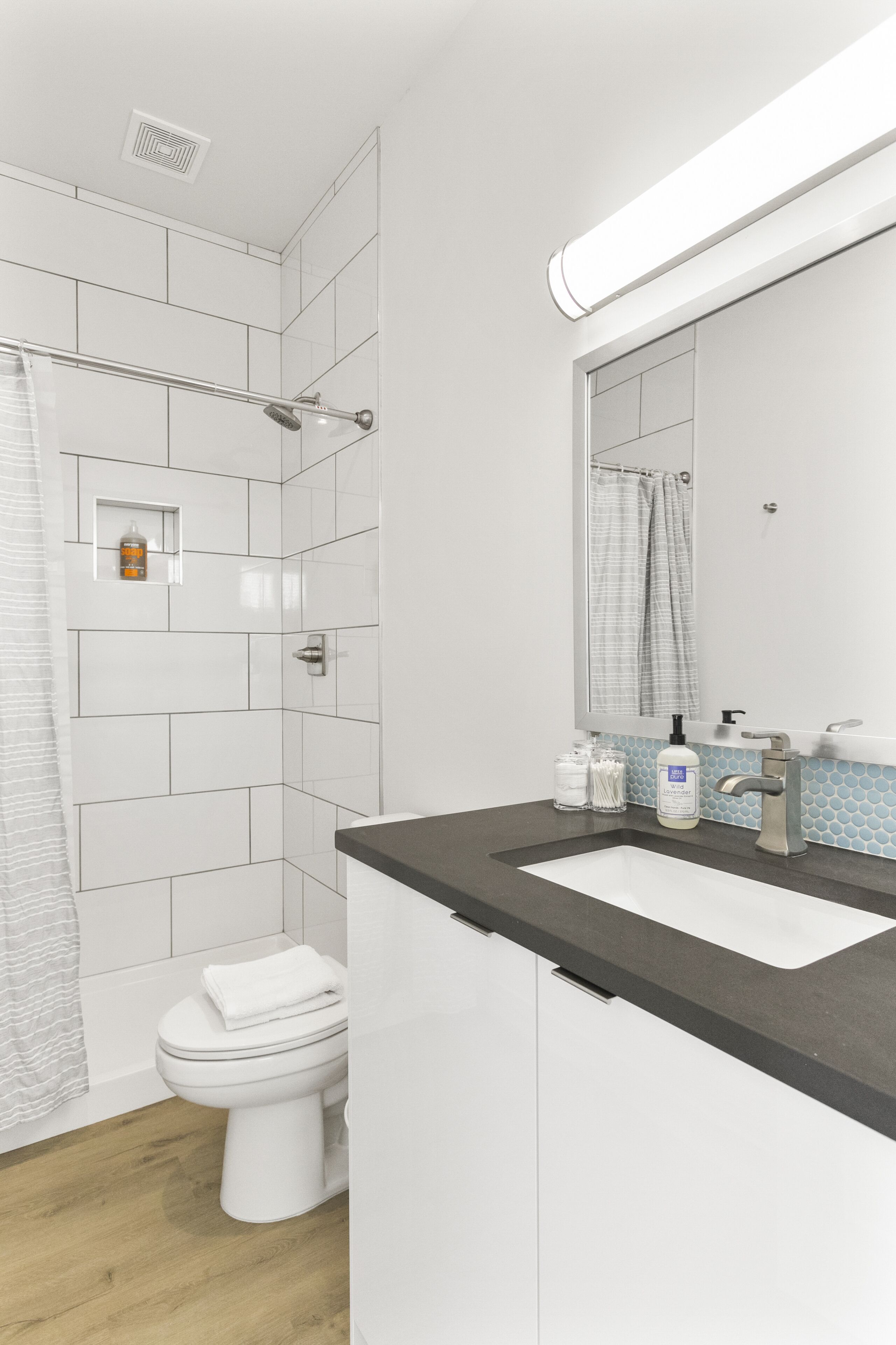 A modern bathroom with white tiles, a black countertop, a white toilet, and a shower area.
