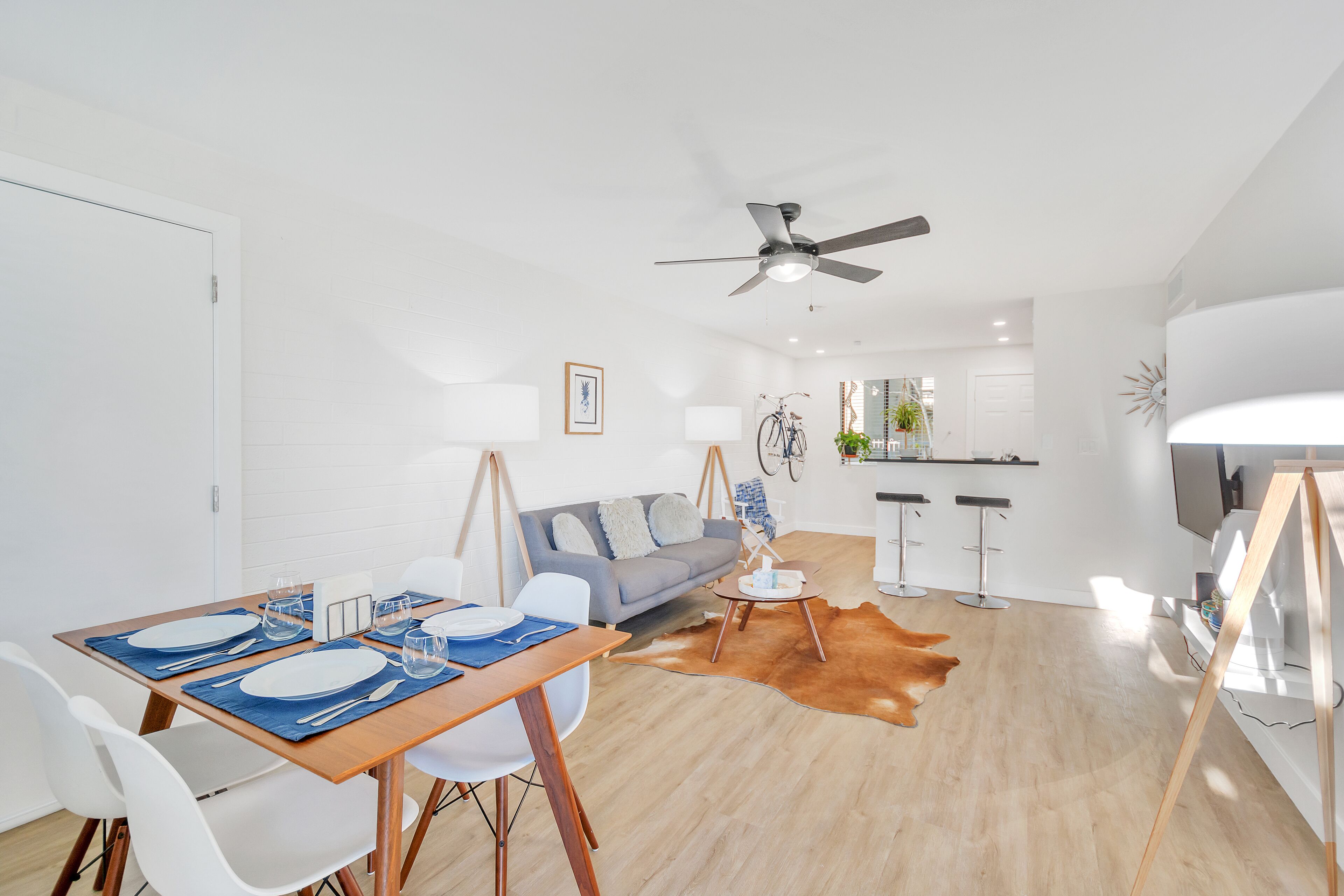 A modern living room with a dining area, a sofa, a ceiling fan, and a kitchen in the background.