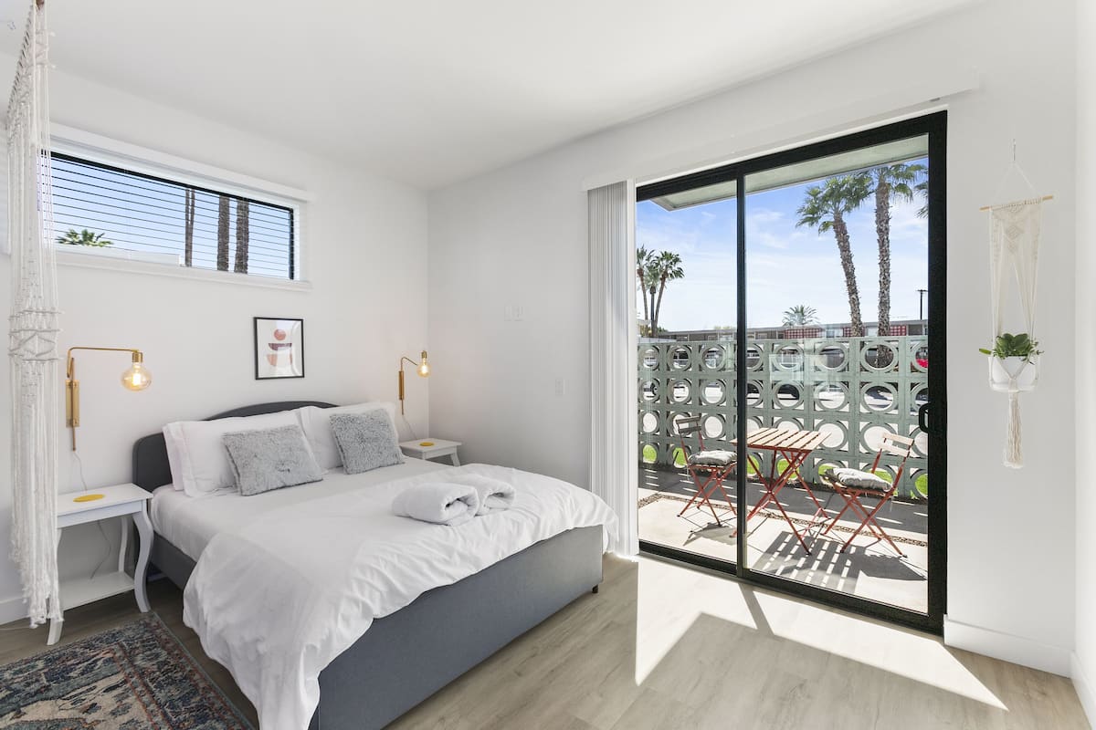 A modern bedroom with a large bed, bedside tables, a nightstand, and a view of the outdoor area through a sliding glass door.