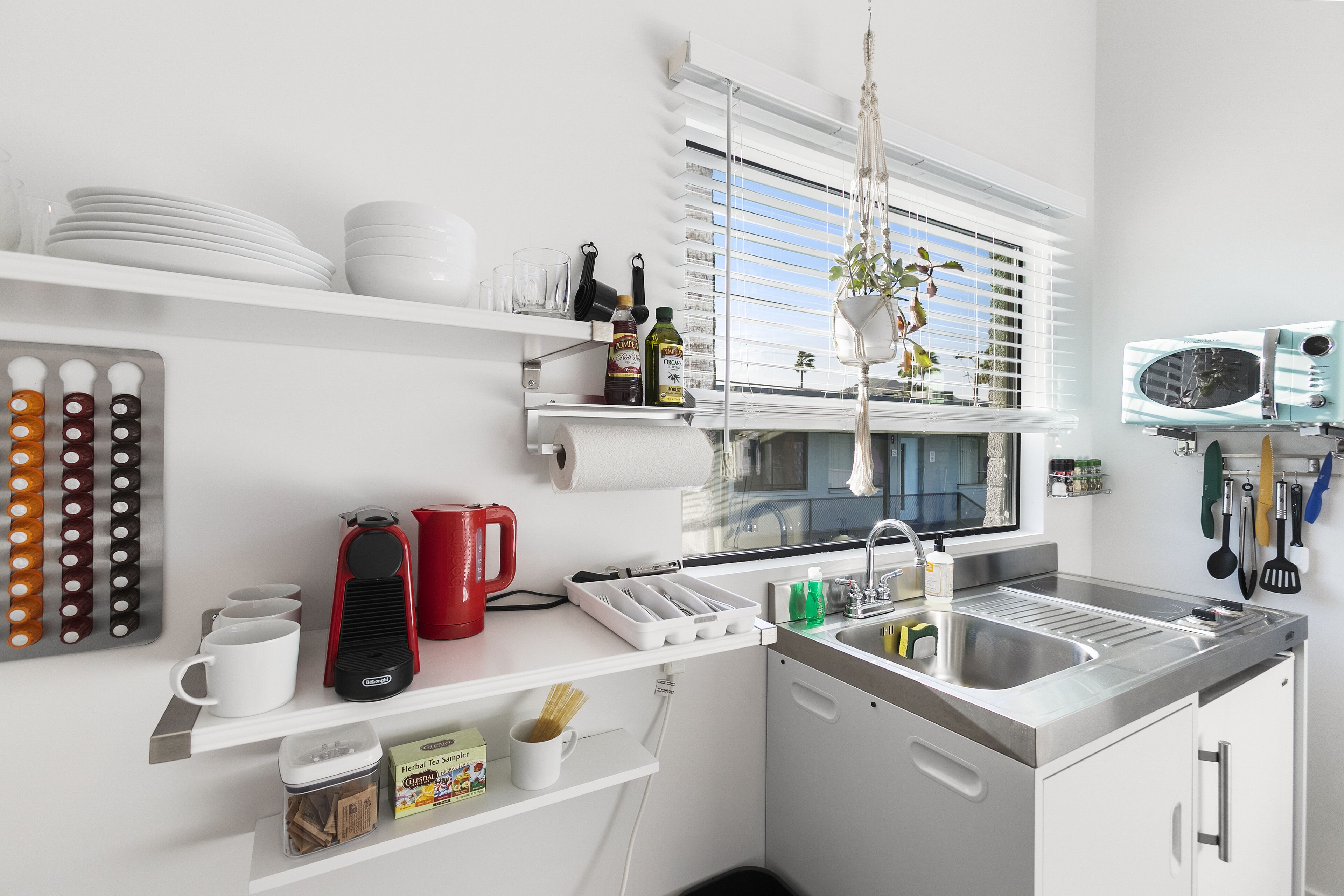 Una cocina moderna con armarios blancos, un lavamanos de acero inoxidable y diversos utensilios y electrodomésticos.
