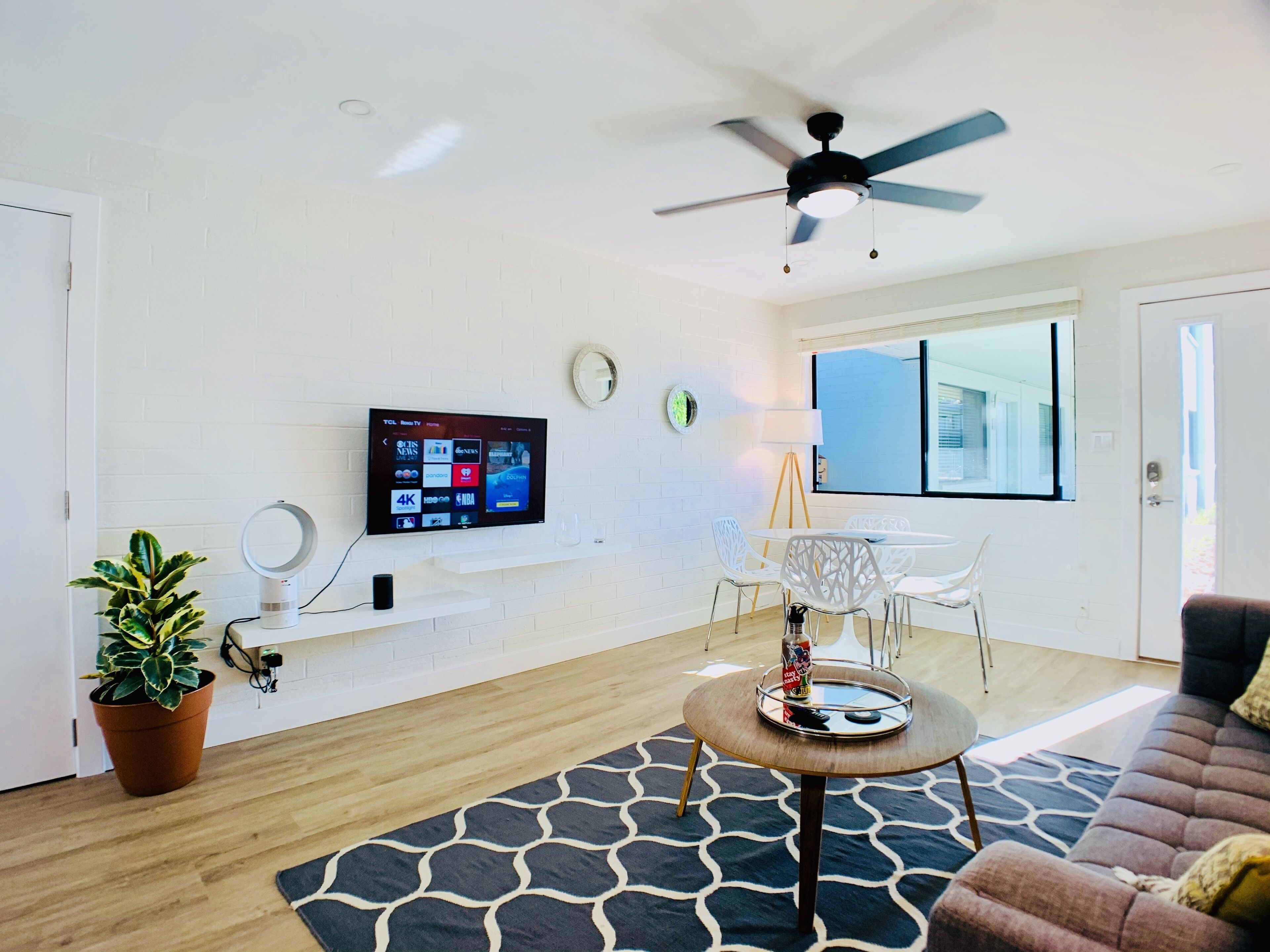 A modern living room with a flat-screen TV, a ceiling fan, a potted plant, a round table with a tray, and a sofa.
