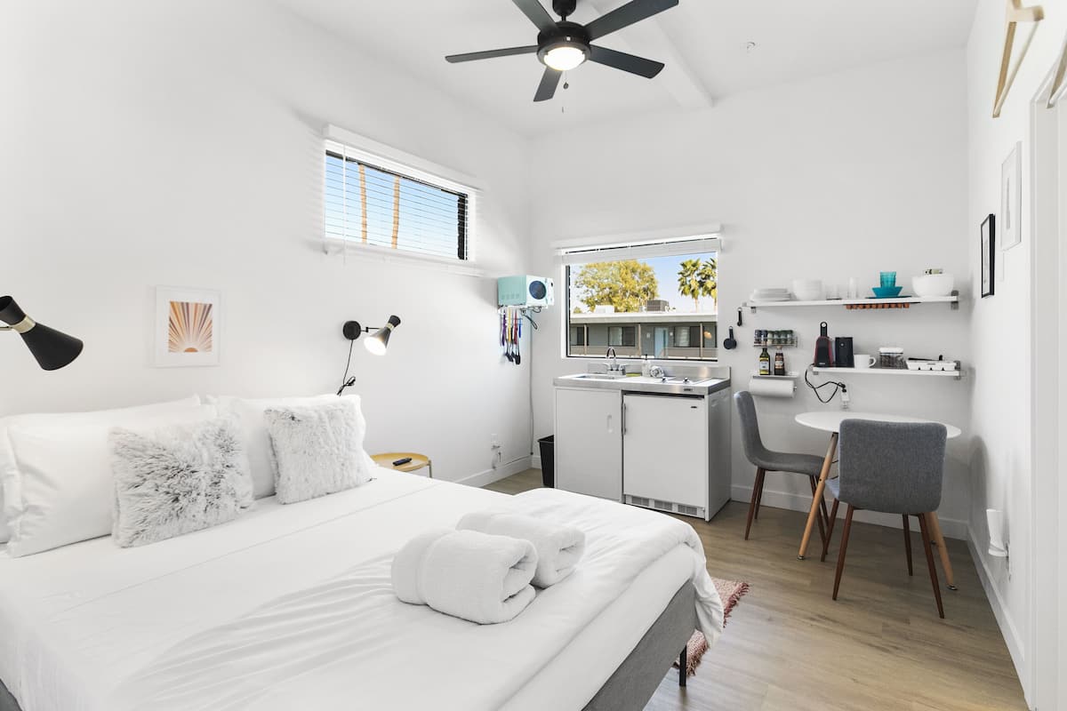 A modern, well-lit bedroom with a bed, bedside table, and a desk area with a chair.
