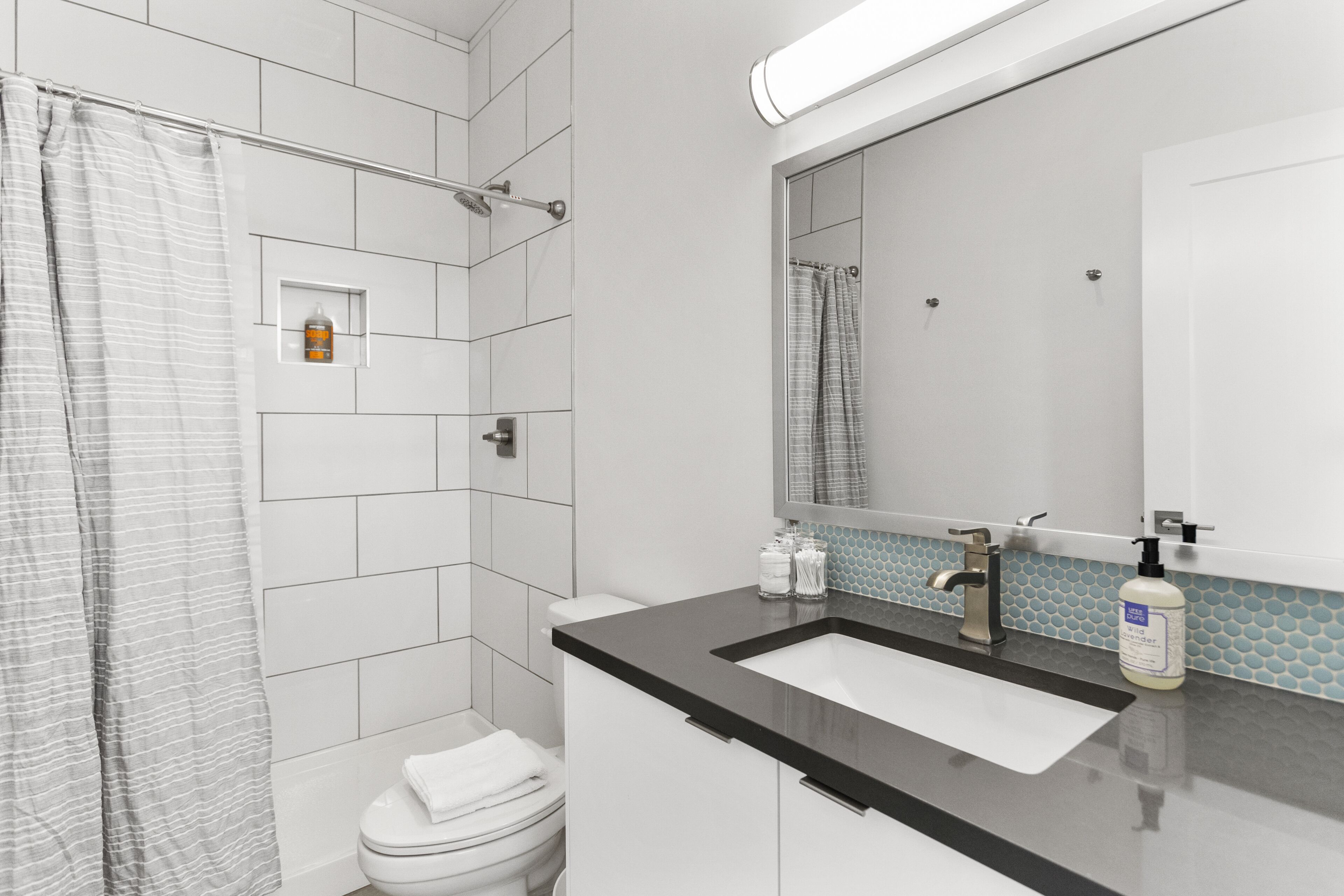 A modern bathroom with a shower, toilet, sink, and a large mirror.