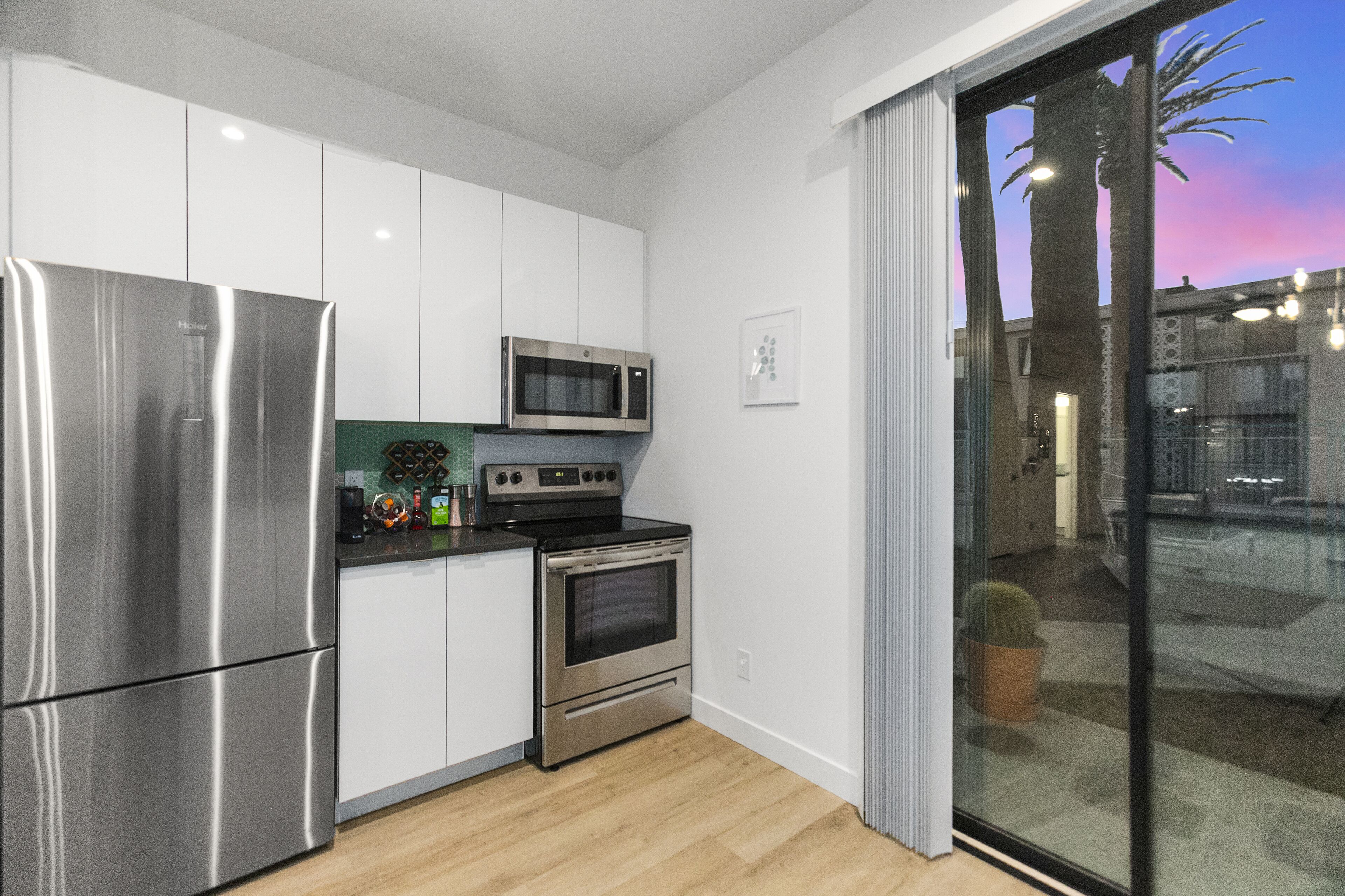 Une cuisine moderne dotée d’appareils électroménagers en acier inoxydable, de meubles blancs et d’une porte-fenêtre coulissante donnant sur un espace extérieur.