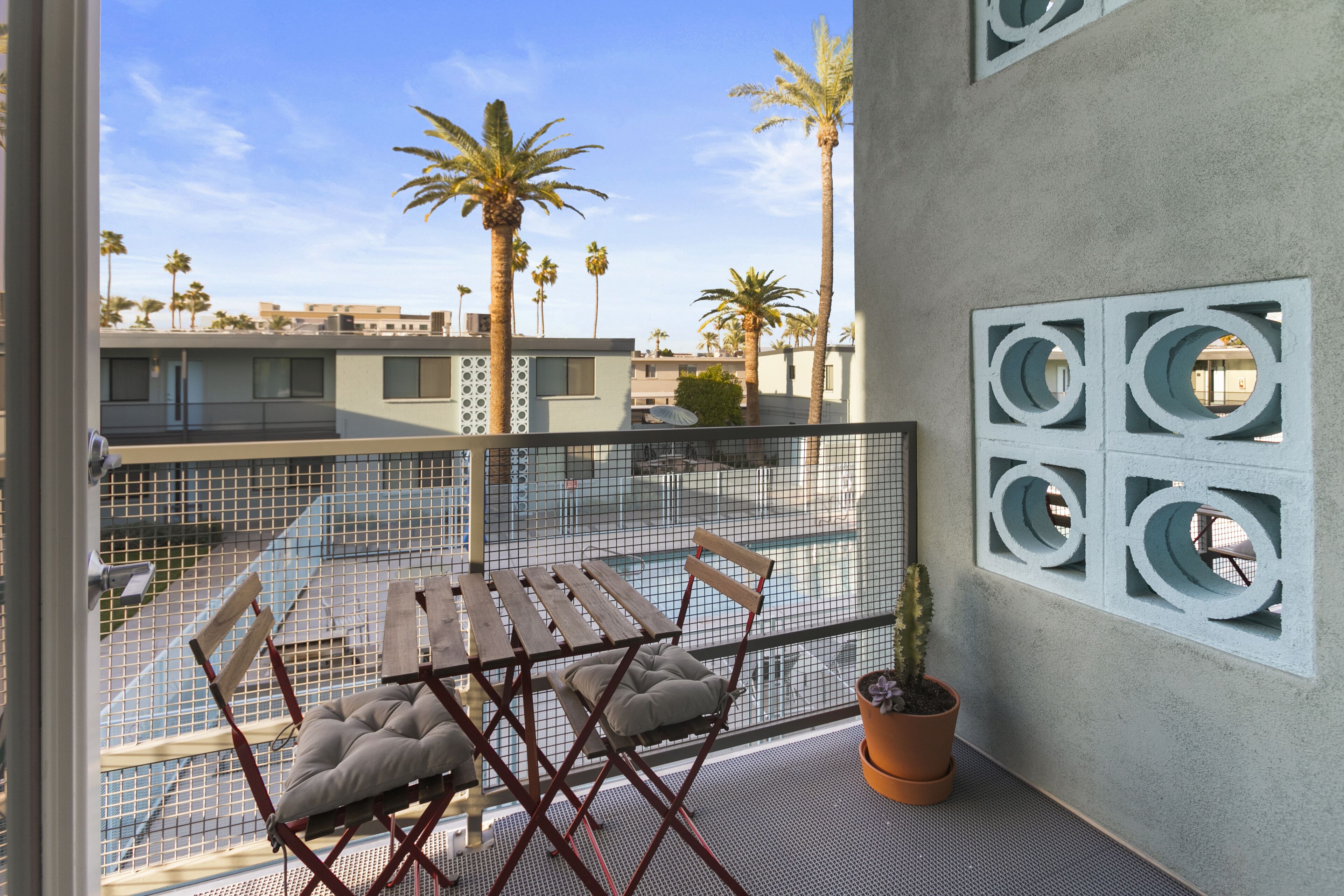 Ein Balkon mit Tisch und Stühlen, einer Topfpflanze und Blick auf Palmen und Gebäude.