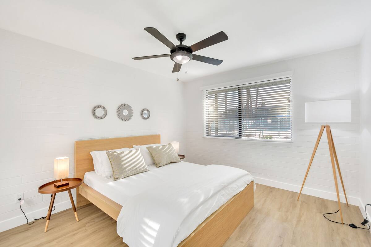 A bedroom with a bed, a ceiling fan, a bedside table with a lamp, and a window with blinds.