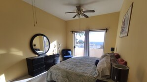 A bedroom with a bed, a dresser, a mirror, a ceiling fan, and a window with a view of the sea. - 2 br 2 ba in gated community w/private beach (Cabo San Lucas)