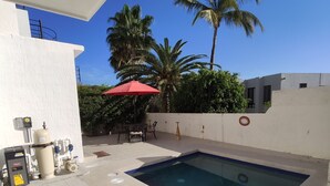 A swimming pool with a red umbrella, surrounded by a white wall and palm trees. - 2 br 2 ba in gated community w/private beach (Cabo San Lucas)