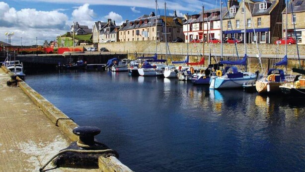 A marina with several boats docked, a stone wall, and buildings in the background. - Taid's Retreat Silversands Cove Beach Lossiemouth (Lossiemouth)