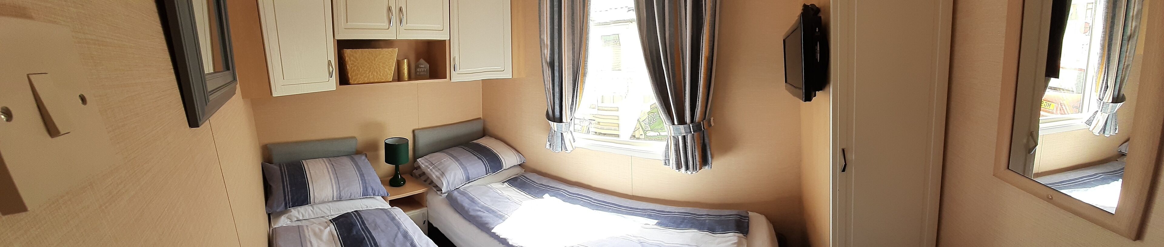 A compact room with two beds, a small table, and a TV mounted on the wall.