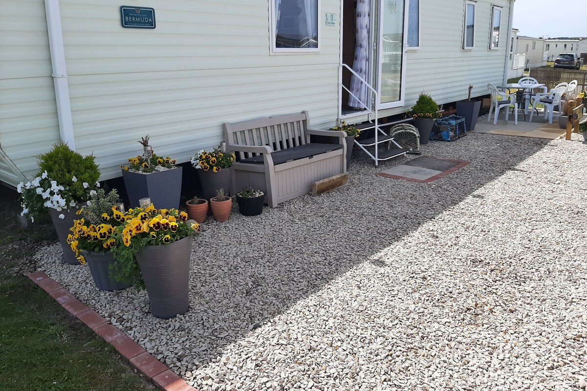 A mobile home with a porch area featuring potted plants, a bench, and outdoor furniture.