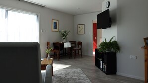 A living room with a sofa, a dining table with chairs, a TV mounted on the wall, and a potted plant.