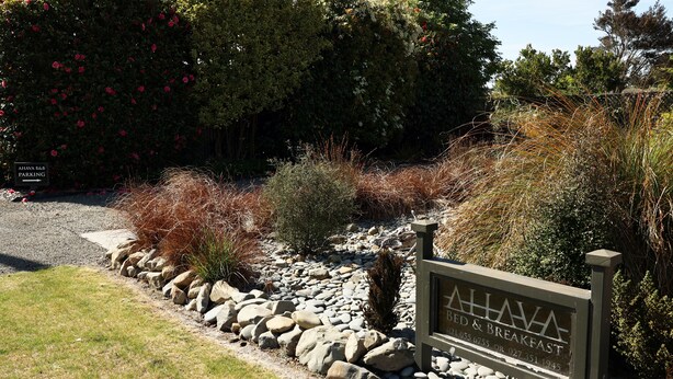 A sign for 'AHAVA BED & BREAKFAST' with a gravel path and rocks leading to the entrance.