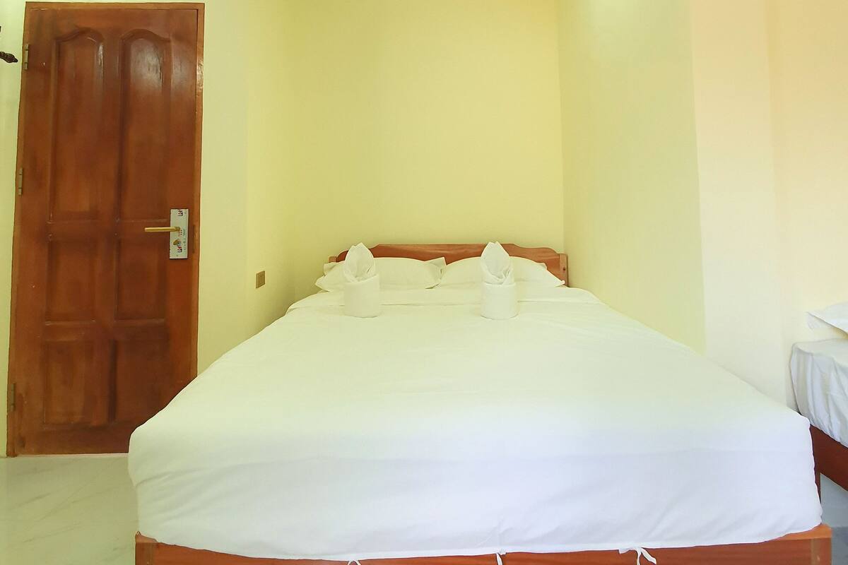 Una cama bien hecha con sábanas blancas y dos toallas, una puerta de madera y una pared de color claro.
