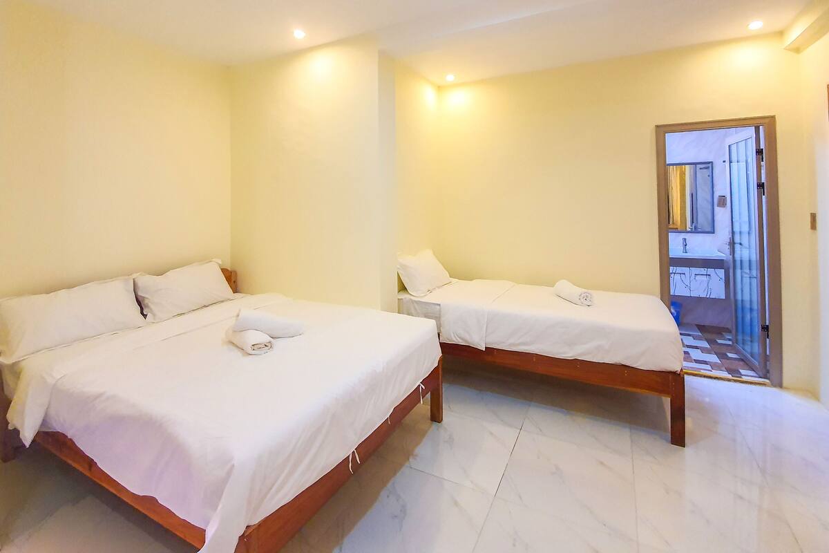Una habitación de hotel con dos camas individuales, un baño con espejo y lavabo, y piso de baldosas.
