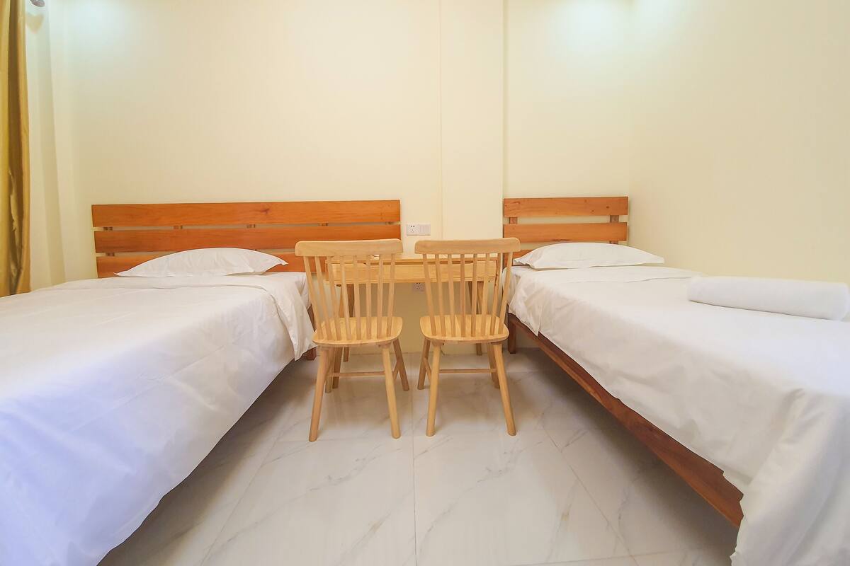 Habitación de hotel con dos camas individuales, una mesa de madera con sillas y una pared blanca lisa.