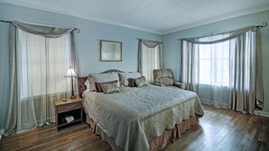 A bedroom with a large bed, a nightstand, a chair, and a window with curtains. - 7 minutes from Providence Farm, MS Blues Trail and The Petrified Forest! (Flora)