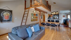 A spacious living area with a wooden staircase, a dining table with chairs, and a kitchen in the background. - Bright Downtown Telluride Condo - Steps to Lift! (Telluride)