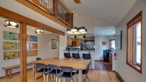 A spacious dining area with a wooden table and chairs, a kitchen in the background, and artwork on the walls. - Bright Downtown Telluride Condo - Steps to Lift! (Telluride)