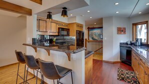 A kitchen with wooden cabinets, a central island with bar stools, stainless steel appliances, and a patterned rug. - Bright Downtown Telluride Condo - Steps to Lift! (Telluride)