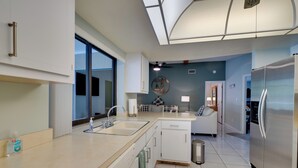 Een moderne keuken met witte kasten, roestvrijstalen apparatuur en een groot raam dat voor natuurlijk licht zorgt.