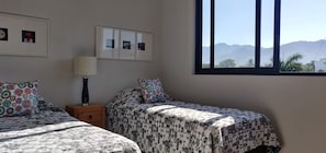 A bedroom with two beds, a nightstand, a lamp, and a window with a mountain view.