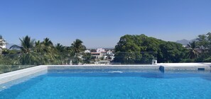 A clear blue swimming pool with tiled edges, surrounded by lush greenery and palm trees.