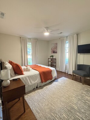 Een hotelkamer met een bed, een bureau, een stoel, een televisie en een plafondventilator.