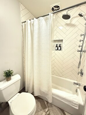 Een badkamer met een wit toilet, een douche met regenstortdouche en een betegelde muur met een herringbone patroon.