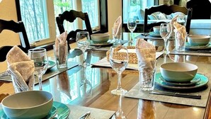 Una mesa de comedor dispuesta con varios cuencos, vasos y cubiertos, sobre una mesa de madera rodeada de sillas.