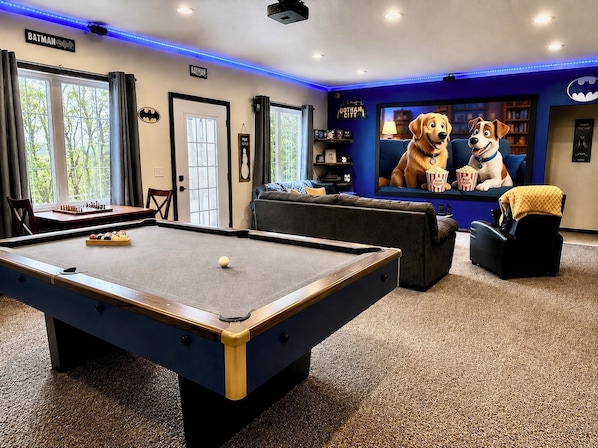 A pool table, a sofa, a television, and a dog statue in a room with blue accents and a Batman sign.