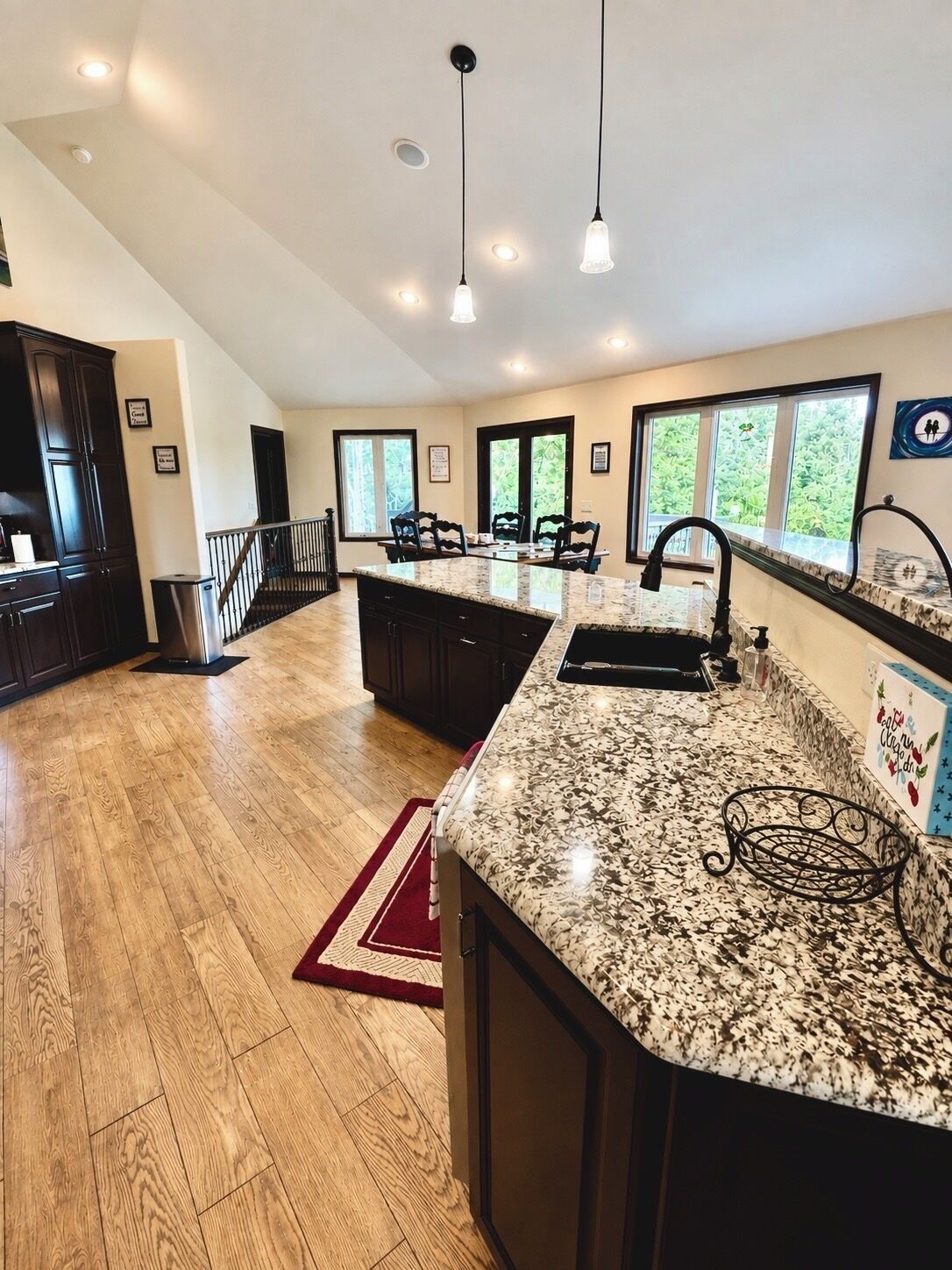A spacious kitchen with a large island, dark cabinetry, and a red rug.
