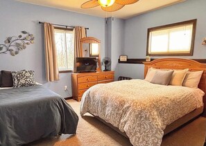 A bedroom with two beds, a dresser, a TV, and a window with curtains.