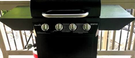 Una parrilla de gas Char-Broil con cuatro perillas de control, una repisa lateral y un tanque de gas.