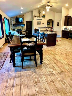 A spacious dining area with a large wooden table and chairs, a stone accent wall, a kitchen with granite countertops, and a fireplace.