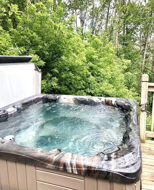 A hot tub on a wooden deck surrounded by lush greenery.